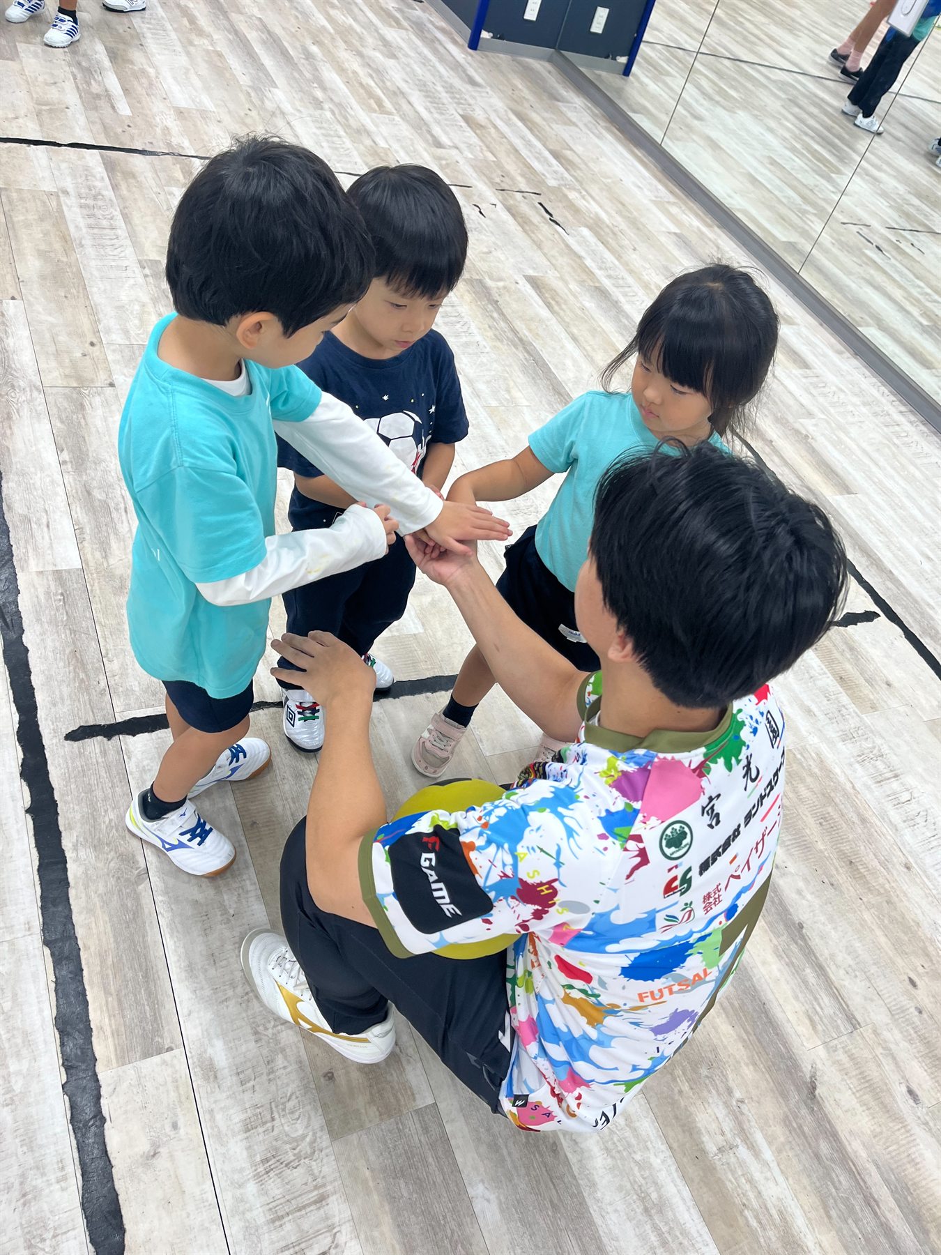 Seiya Kitano and the children bringing their hands together in a team huddle